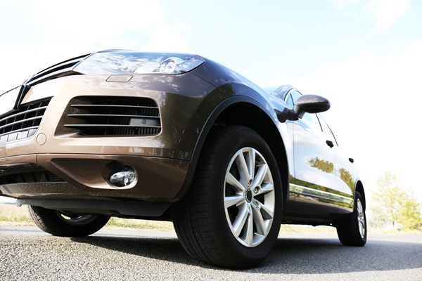 Low-angle view of a brown SUV driving or parked on a road with clear skies and a distant tree in the background.