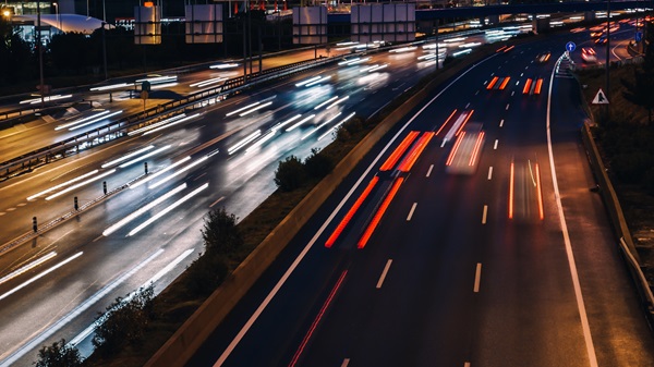 Blurred lights of speeding cars on a multi-lane highway at night, creating streaks of light to indicate fast-moving traffic.