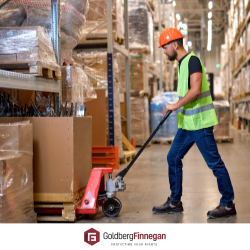 Warehouse employee in safety vest, lifting boxes with a dolly