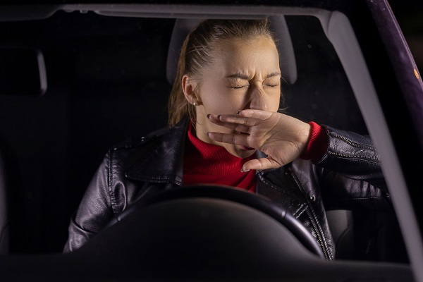 Female driver yawning behind the wheel, appearing tired and struggling to stay awake while driving at night.